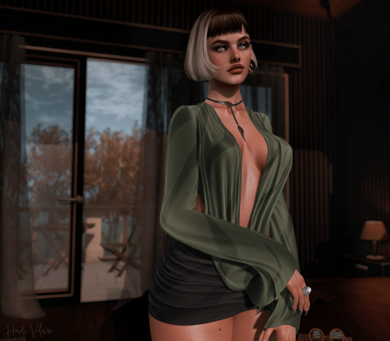 A stylish woman with a sleek blonde bob and dark bangs poses in a dimly lit, elegant room, wearing an olive-green blouse, a black skirt, and delicate jewelry. Her striking gaze and composed expression create a mysterious, sultry mood, while warm lighting and autumn foliage outside the windows add to the cinematic atmosphere.